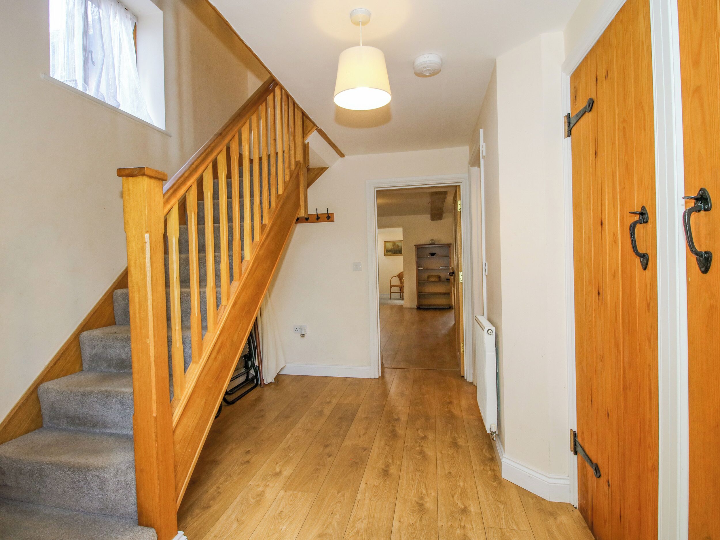 Una escalera de madera con barandilla que lleva a una plataforma, un pasillo con piso de madera y una puerta con picaporte.