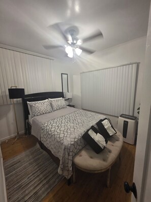 A bedroom with a bed, bedside table, lamp, ceiling fan, radiator, and a bench. - Cozy 1-Bedroom Urban Retreat with Modern Comforts (Los Angeles)
