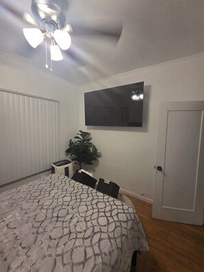 A bedroom with a bed, a ceiling fan, a TV, a door, and a plant. - Cozy 1-Bedroom Urban Retreat with Modern Comforts (Los Angeles)