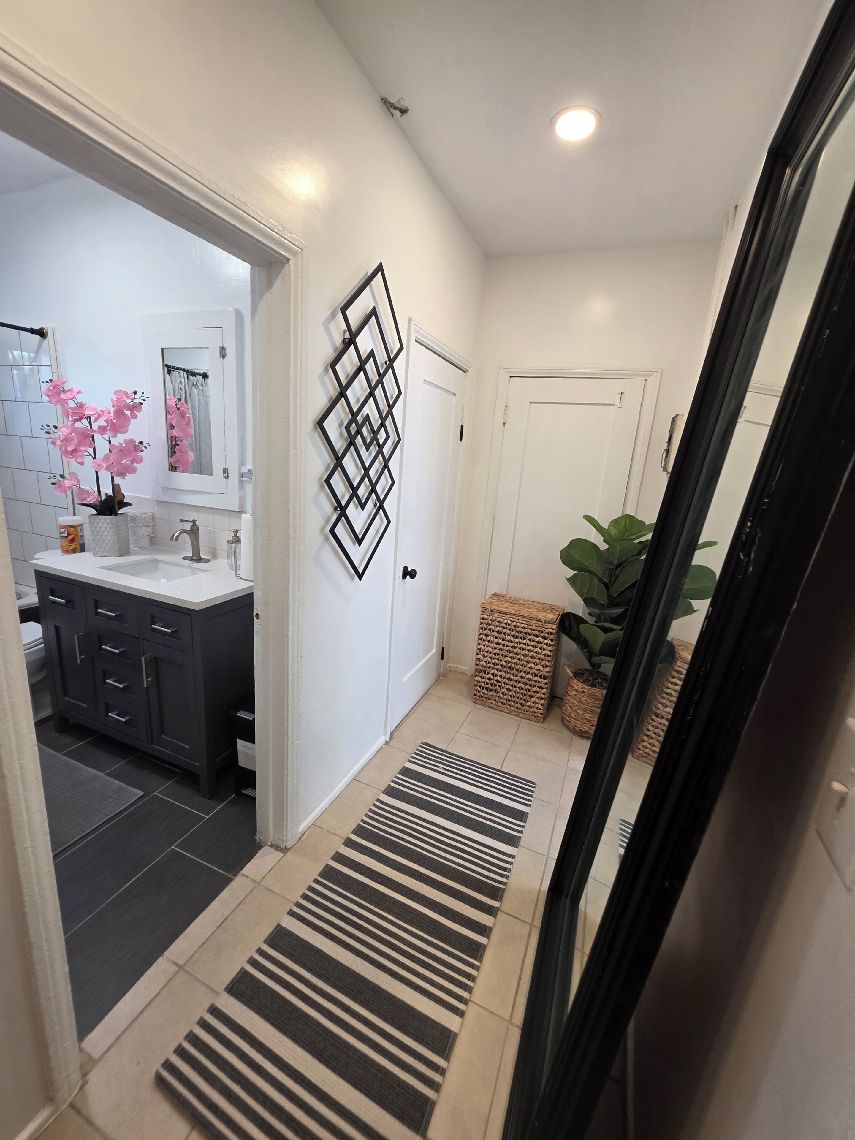 A modern bathroom with a dark grey vanity, white sink, and a decorative mirror.