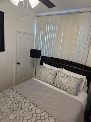 A bedroom with a bed, a door, a ceiling fan, and a window with blinds. - Cozy 1-Bedroom Urban Retreat with Modern Comforts (Los Angeles)