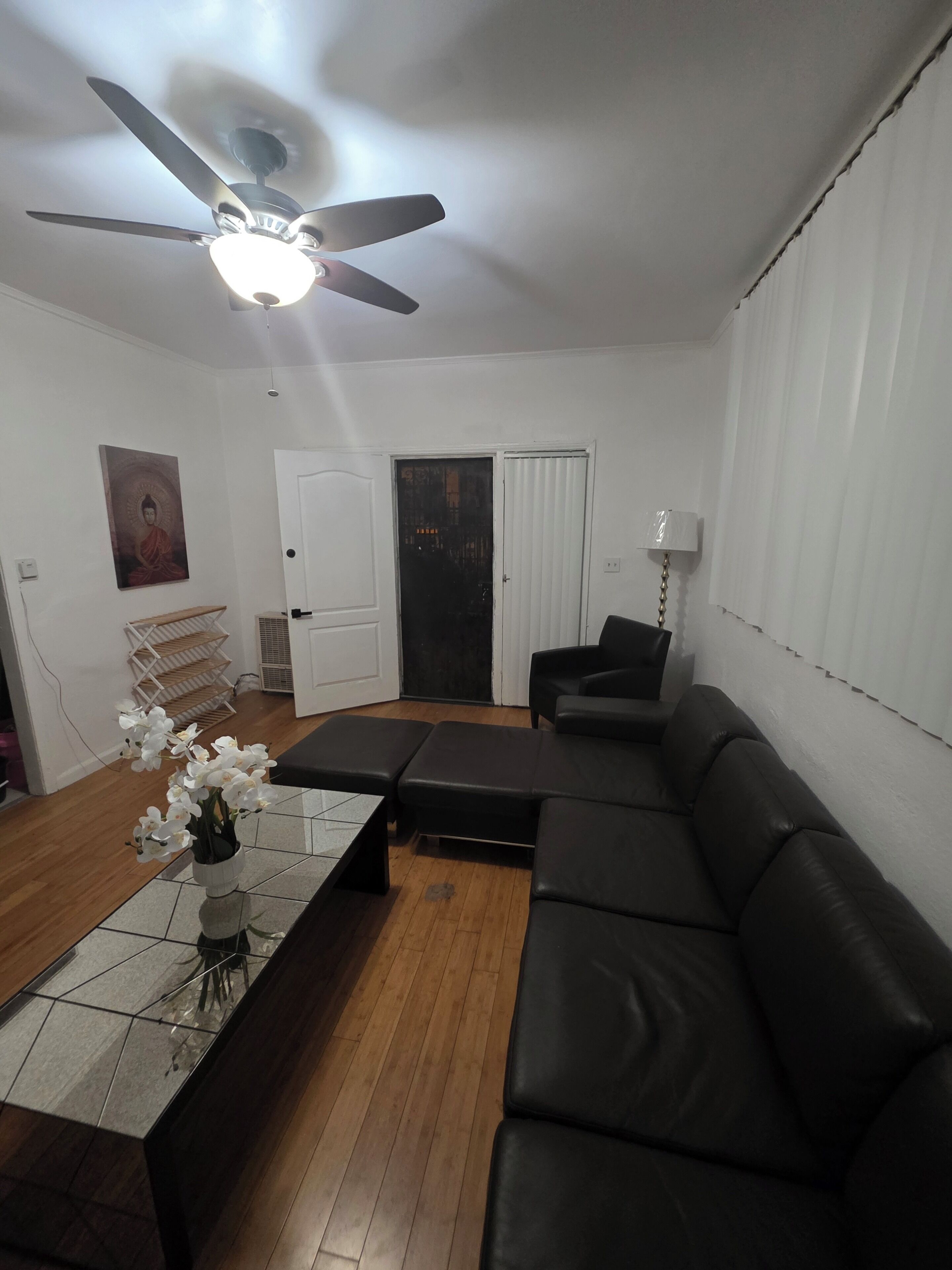 A living room with a ceiling fan, a black leather sofa, a coffee table, and a door leading to another room.