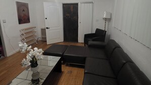 Un salon doté d’un ventilateur de plafond, d’un canapé en cuir noir, d’une table basse et d’une porte donnant sur une autre pièce.