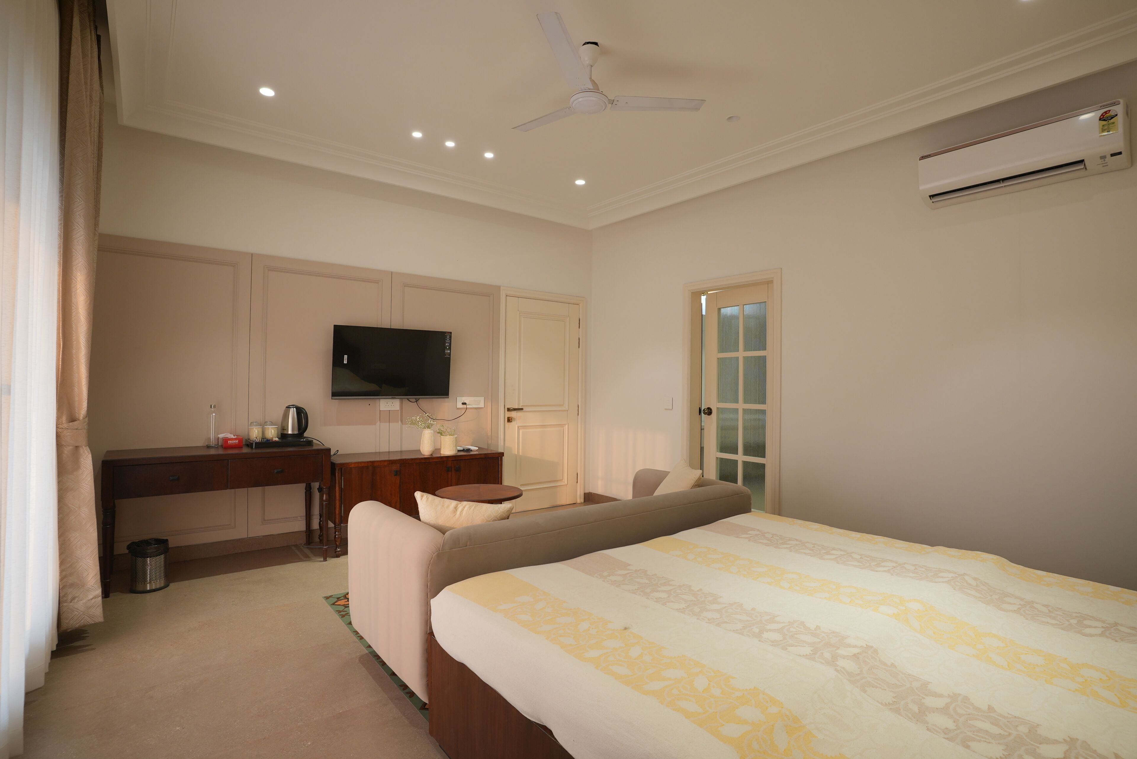 A hotel room with a bed, a desk, a television, an air conditioner, and a door.