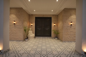 A hallway with a patterned tile floor, a dark double door, and wall-mounted lights.