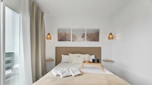 Et hotelværelse med en stor seng, et natbord, bakke med genstande og udsigt til det fri.