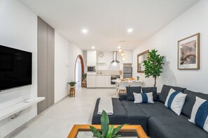Ein modernes Wohnzimmer mit einem Flachbildfernseher, einer Couch, einem Couchtisch und einem Essbereich im Hintergrund.