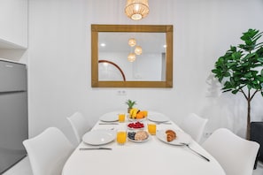 Ein moderner Essbereich mit einem weißen Tisch, gedeckt für ein Frühstück, inklusive Früchte, Saft und Gebäck.