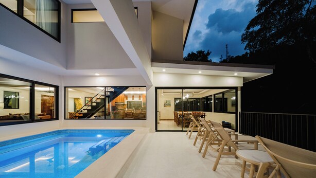 Ein modernes Haus mit Swimmingpool, Holzliegen und einer Treppe, die zu einer oberen Ebene führt.