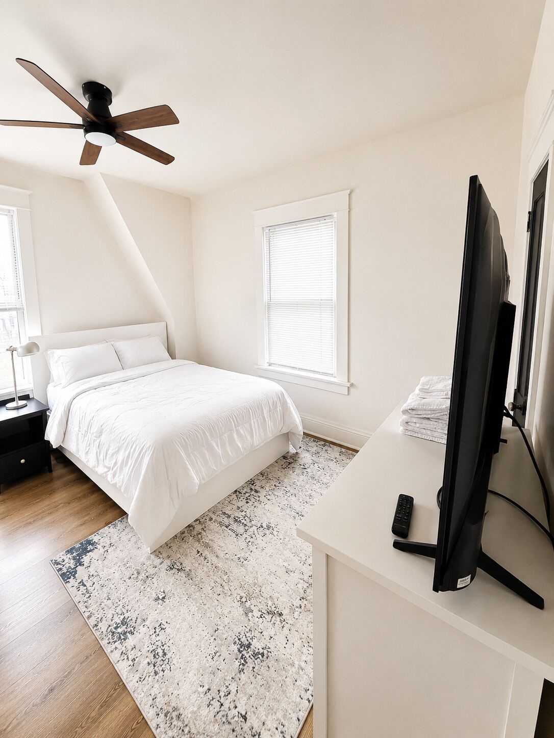 Ein Schlafzimmer mit Bett, Schreibtisch, Computer, Deckenventilator und Fenster.