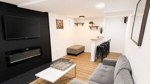 Una sala de estar moderna con un televisor de pantalla plana, una chimenea, un sofá gris y piso de madera.