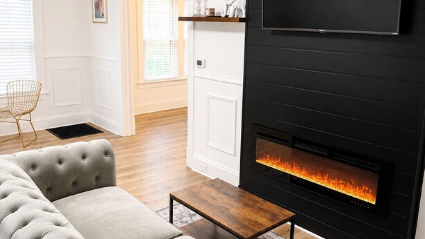 Una sala de estar con un sofá gris, una chimenea, un televisor montado y una mesa de centro de madera.