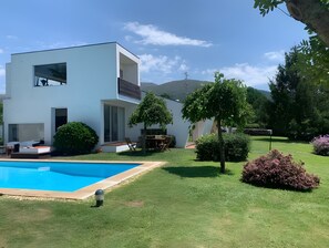 Ein modernes, zweistöckiges Haus mit Swimmingpool, Terrasse und Gartenmöbeln sowie einem gepflegten Rasen.