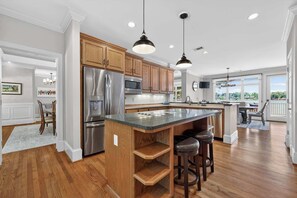 A modern kitchen with wooden cabinets, stainless steel appliances, and a large island with bar stools. - Sandy Cove Cottage- Great Waters Lakefront Luxury (Eatonton)