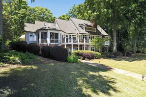 A two-story house with a wrap-around porch, a well-maintained lawn, and mature trees. - Sandy Cove Cottage- Great Waters Lakefront Luxury (Eatonton)