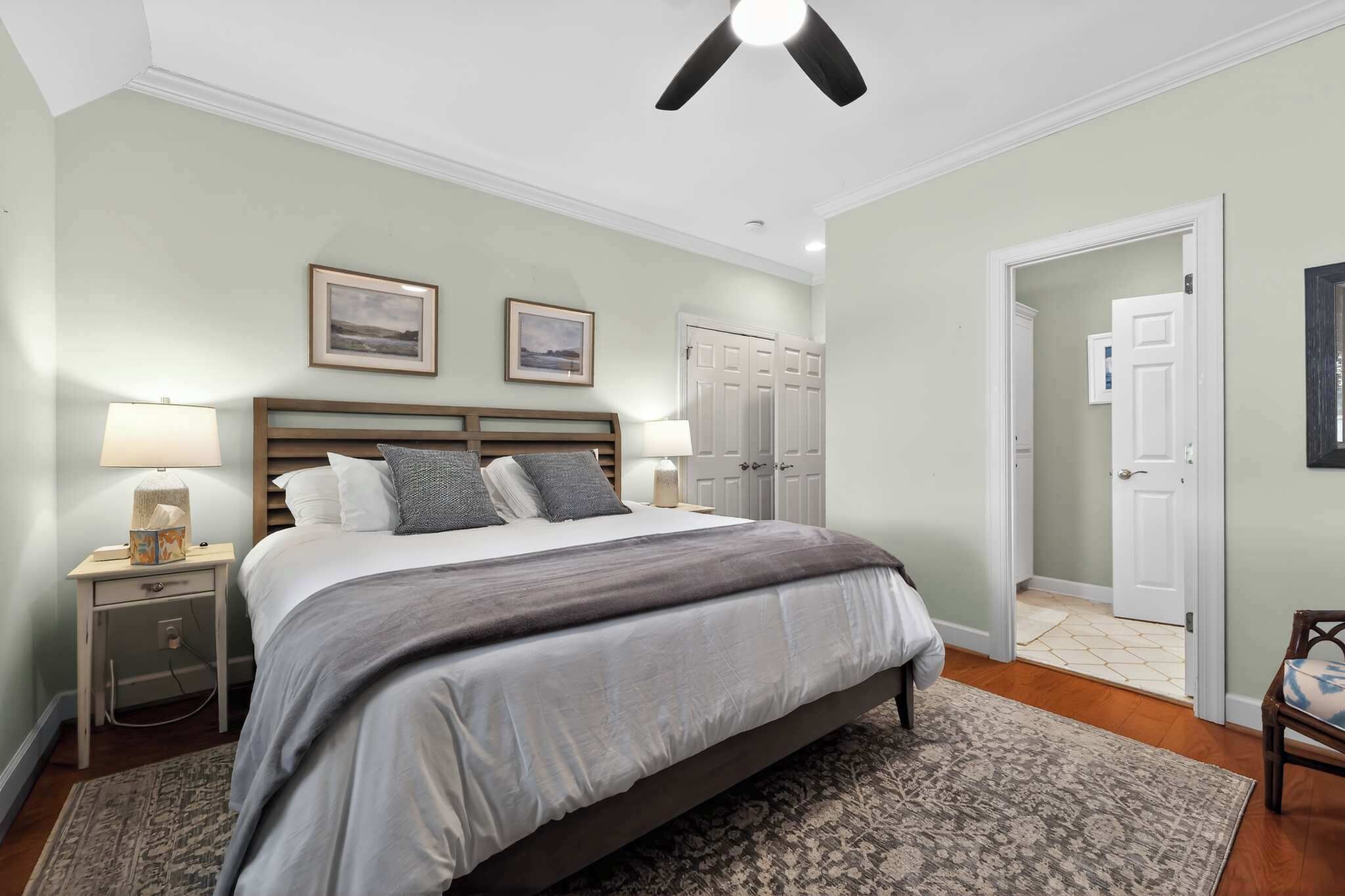 A bedroom with a bed, nightstands, a ceiling fan, a door, and a hallway.