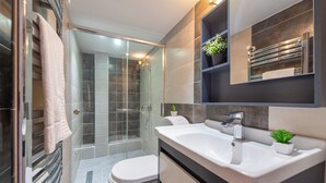 Un baño moderno con cabina de ducha de vidrio, inodoro blanco, un lavamanos grande con espejo y dos macetas.