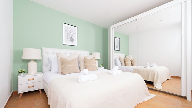 Un dormitorio moderno con una cama grande, una mesita de noche, un espejo y una pared verde.