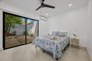 A bedroom with a bed, a nightstand, a ceiling fan, and a view of a garden through a sliding door. - New 4BR Retreat w Saltwater Pool | Walk to Beach & Town (Tamarindo)