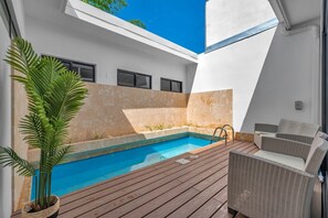 A modern outdoor pool area with a wooden deck, a lounge chair, and a potted plant. - New 4BR Retreat w Saltwater Pool | Walk to Beach & Town (Tamarindo)