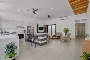 A modern kitchen with a marble island, bar stools, and a dining area with a sofa and coffee table. - New 4BR Retreat w Saltwater Pool | Walk to Beach & Town (Tamarindo)