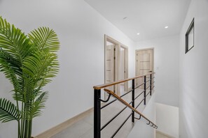 A staircase with wooden handrails, white walls, and a potted plant. - TW9 4BR Retreat w Saltwater Pool Walk to Beach & Town (Tamarindo)