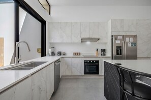 A modern kitchen with a built-in oven, a stainless steel refrigerator, and a black countertop. - TW9 4BR Retreat w Saltwater Pool Walk to Beach & Town (Tamarindo)