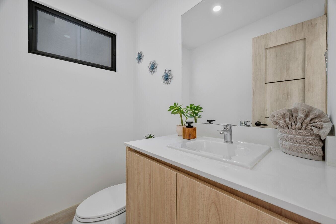 A modern bathroom with a white vanity, a mirror, a sink, a toilet, and decorative wall art.