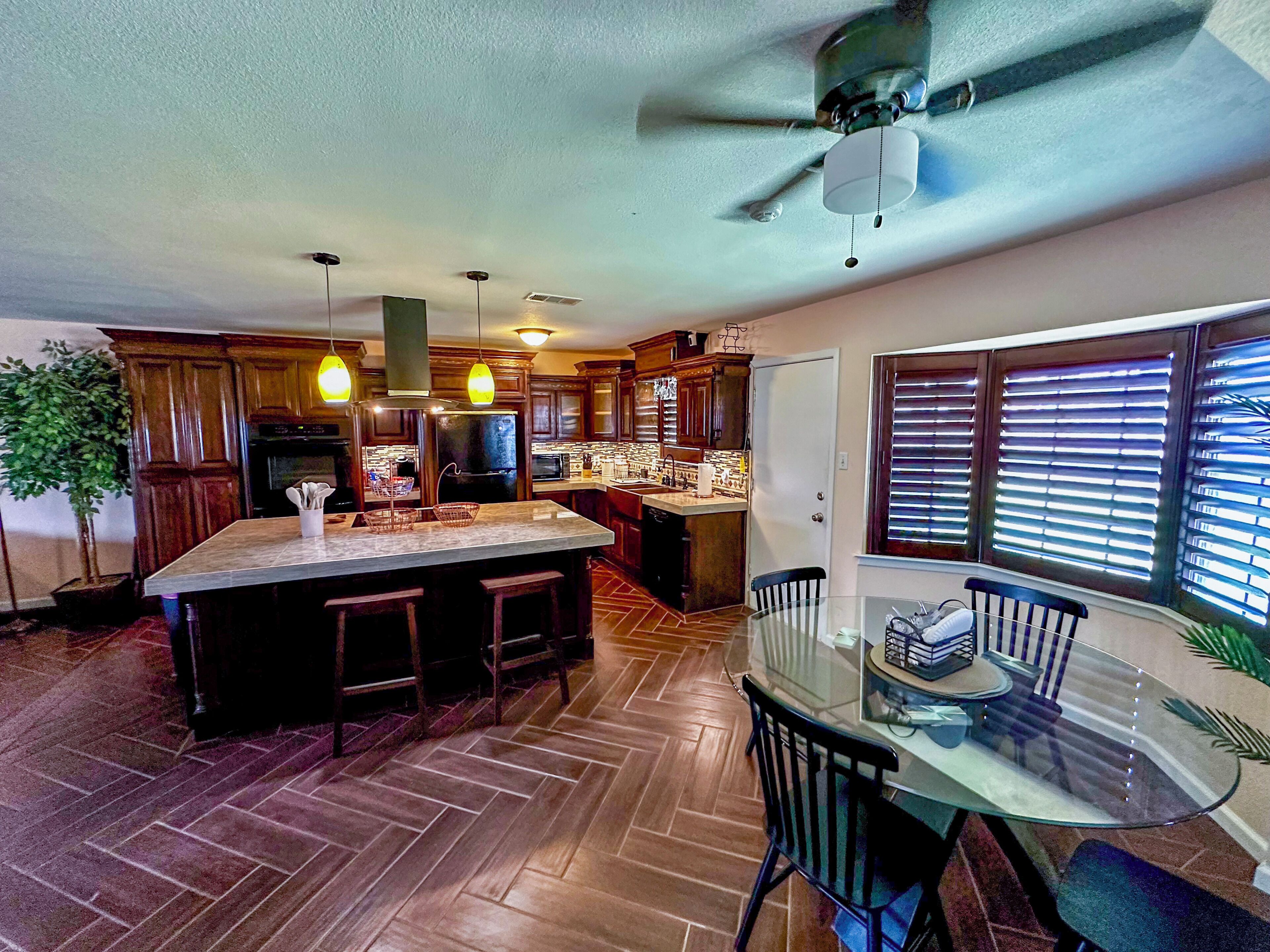 A kitchen with a central island, wooden cabinets, a dining area with a glass table, and a ceiling fan. - 3-bed 2-bath, Casa de Salazar. A true ~ Home Away from Home ~ (Odessa)