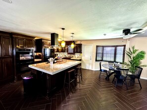 A kitchen with dark wood cabinets, a central island, and a dining area with a table and chairs. - 3-bed 2-bath, Casa de Salazar. A true ~ Home Away from Home ~ (Odessa)