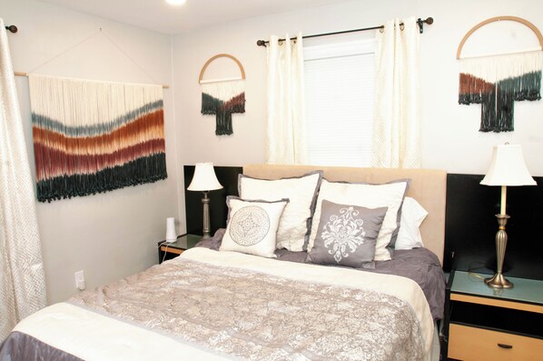 A neatly arranged bedroom with a bed, bedside tables, lamps, and decorative wall hangings. - Coziness in South Broad Ripple (Indianapolis)