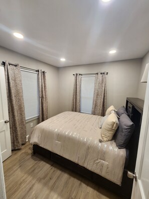 A bedroom with a bed, curtains, a window with blinds, a door, and a ceiling light.