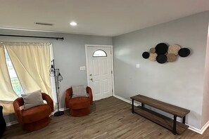 Ein Zimmer mit zwei orangefarbenen Sesseln, einer Bank, einer weißen Tür und einer Wand mit runden Wandbildern.