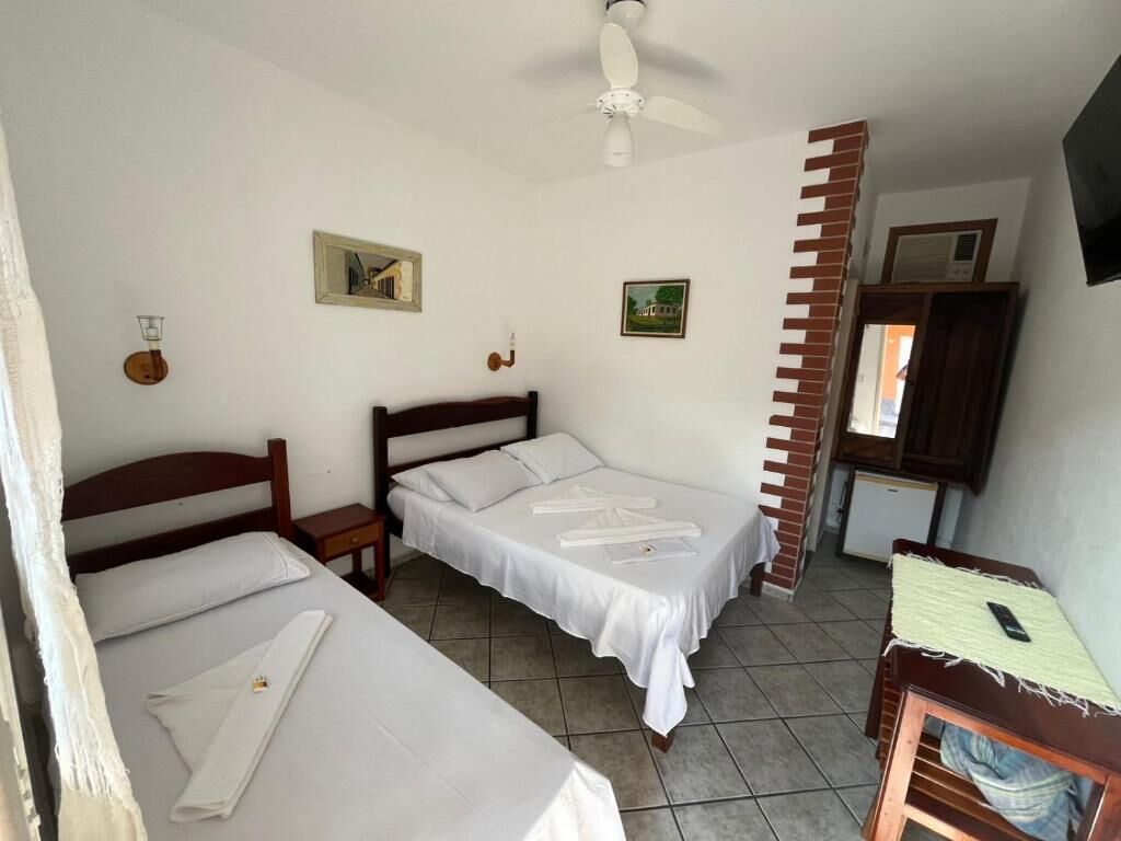 Una habitación con dos camas, ventilador de techo, una mesita y televisor montado en la pared.