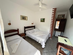 Una habitación con dos camas, ventilador de techo, una mesita y televisor montado en la pared.