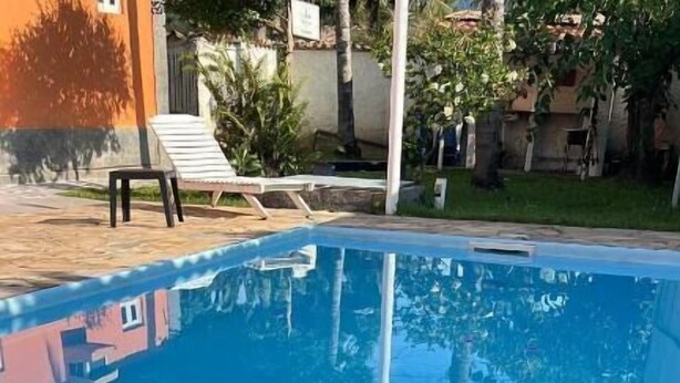 Una piscina con borde de piedra, rodeada de césped y algunos árboles.