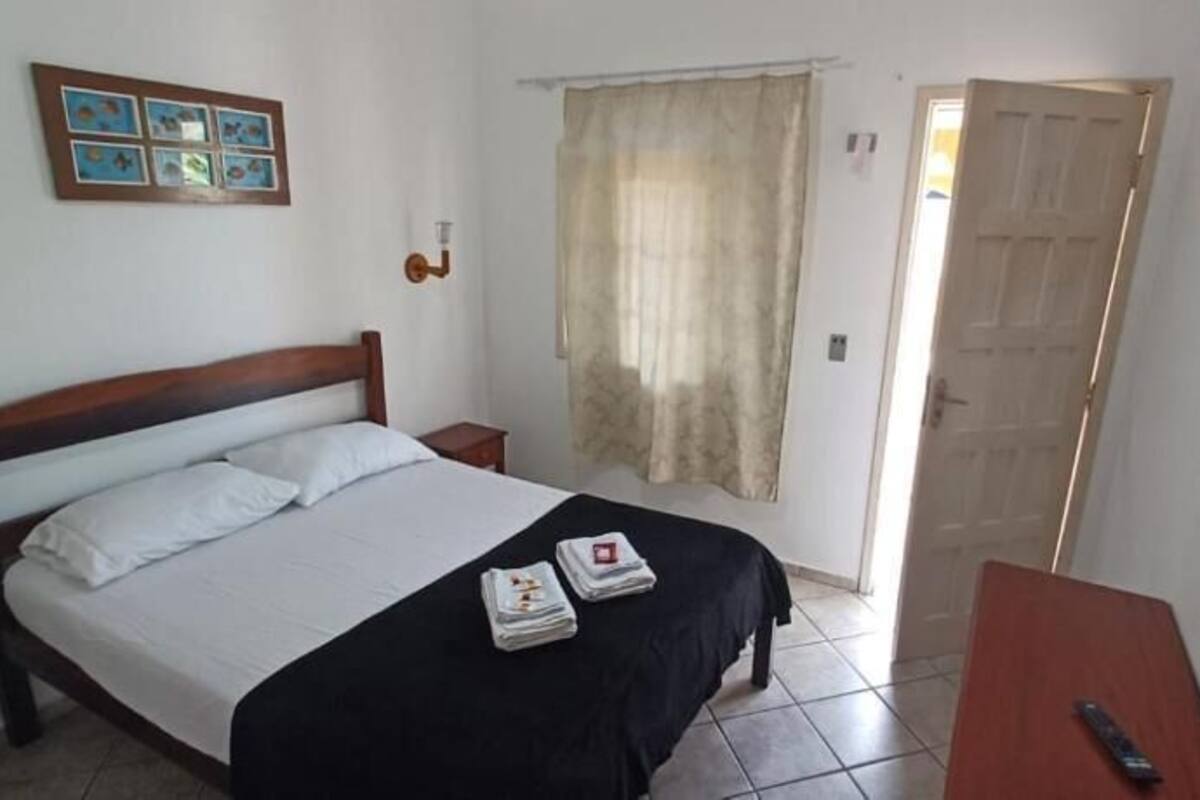 Een slaapkamer met een bed, nachtkastjes, een bureau, een stoel, een deur en een gordijn.