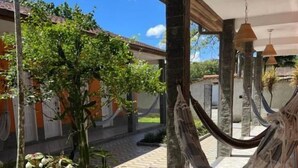 Un espacio exterior techado con una hamaca, suelo de baldosas y plantas en macetas.