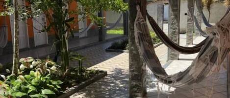 A covered outdoor area with a hammock, tiled flooring, and potted plants.