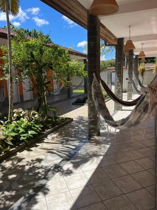 Un espacio exterior techado con una hamaca, suelo de baldosas y plantas en macetas.