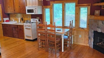 A wooden-paneled kitchen with a stone fireplace, wooden dining table, and chairs.