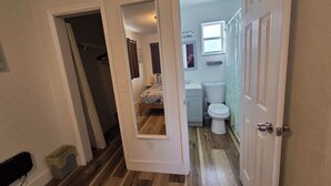 Un couloir mène à une chambre à coucher avec un lit, à une salle de bain avec des toilettes et un lavabo, et à une porte qui donne sur une autre pièce.