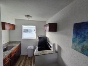 Eine kleine Küche mit Granitarbeitsplatten, einem eingebauten Ofen, einem Fenster und einem Bild an der Wand.