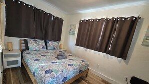 Une chambre à coucher avec un lit, des rideaux, une table de chevet, une lampe et une prise électrique au mur.
