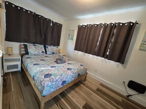 Ein Schlafzimmer mit Bett, Vorhängen, Nachttisch, Lampe und einer Steckdose.