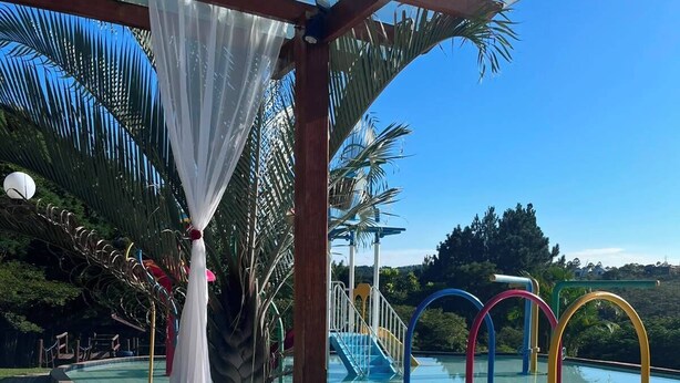 A hot tub with a clear view of the pool and slides, surrounded by palm trees and a wooden pergola.