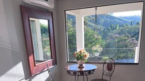 A room with a large window, a round table with chairs, a bathtub, and an air conditioning unit.