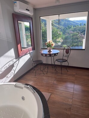 Une pièce dotée d’une grande fenêtre, d’une table ronde avec des chaises, d’une baignoire et d’un appareil de climatisation.