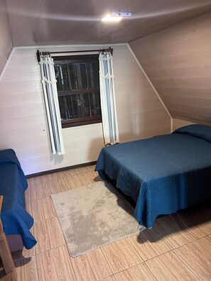 Une petite pièce aux murs inclinés, comprenant un lit simple, une chaise et une fenêtre avec des rideaux.