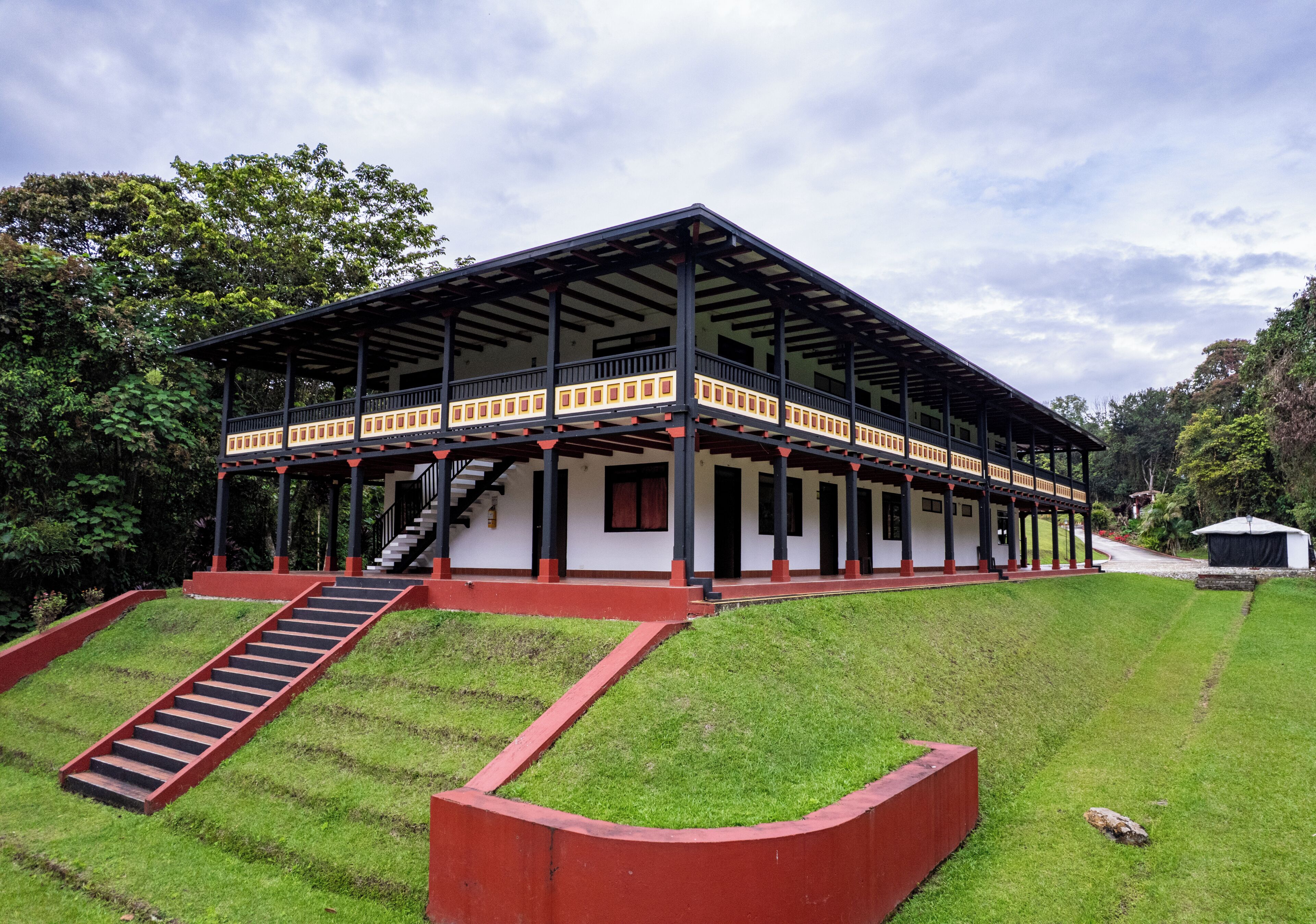 Un edificio con un balcón cubierto, una escalera y un césped.